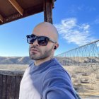 Bald tattooed man in sunglasses with futuristic cityscape and flying vehicle.