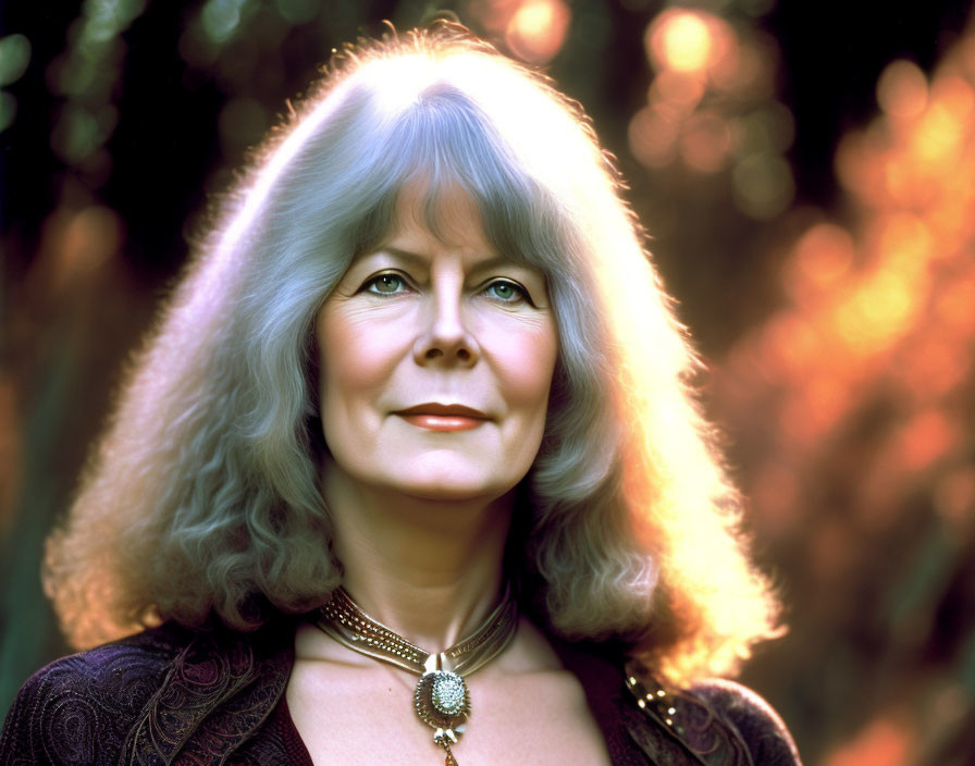 Serene older woman with long silver hair and necklace in dark clothing