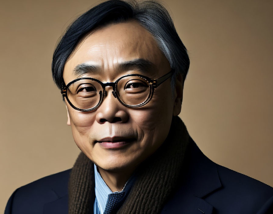 Asian man in round glasses, dark blazer, brown turtleneck on beige background