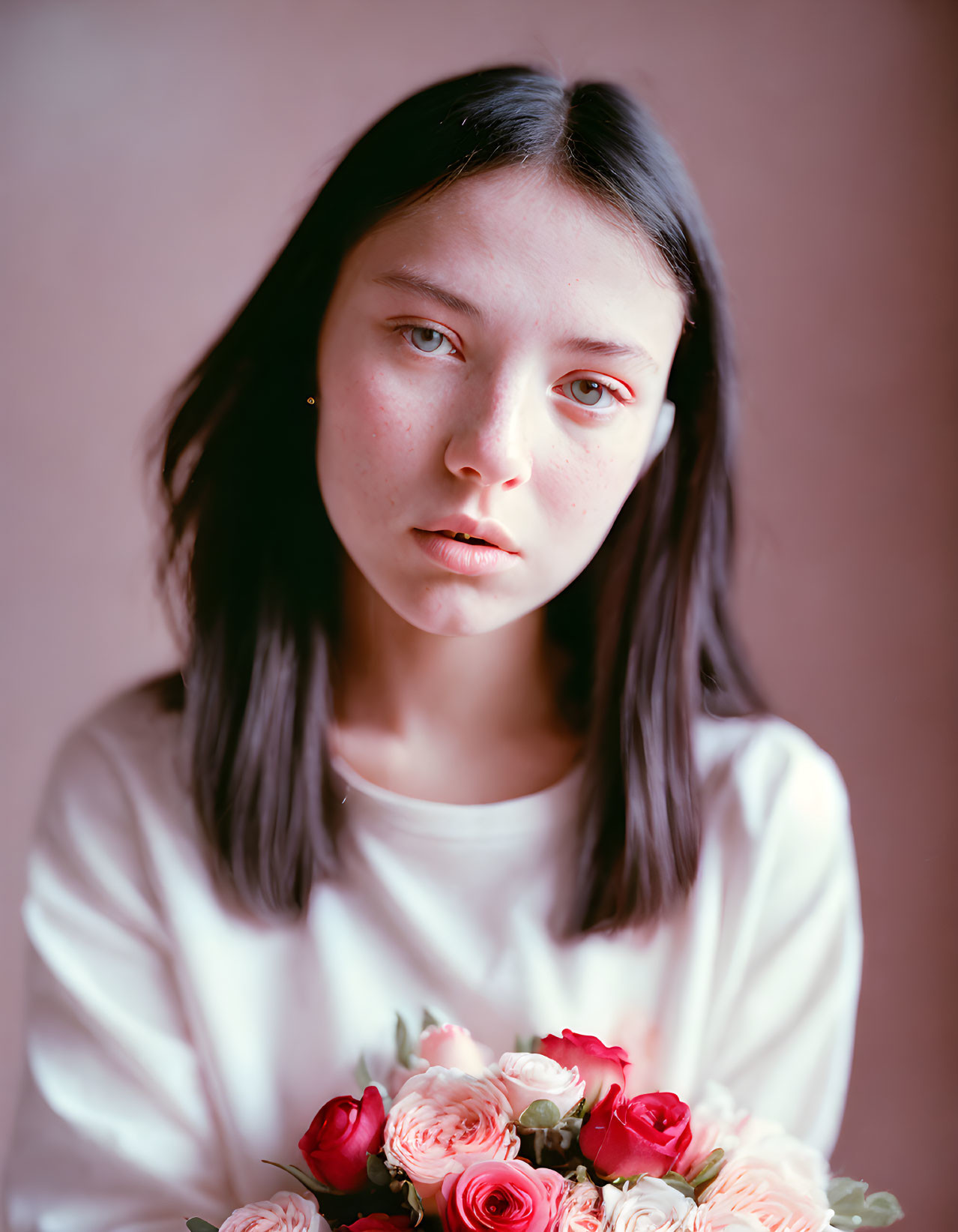 Young woman with dark hair holding pink and red roses on soft-focus background