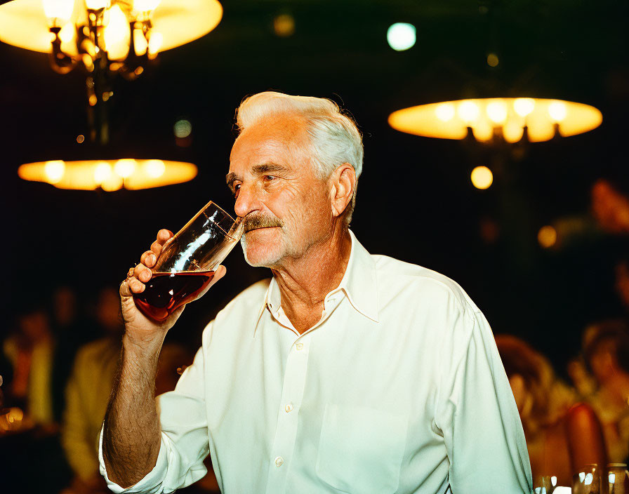 Elderly man with mustache enjoying a drink in white shirt