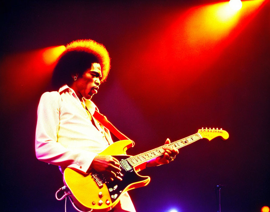 Afro musician plays yellow electric guitar under red and blue stage lights