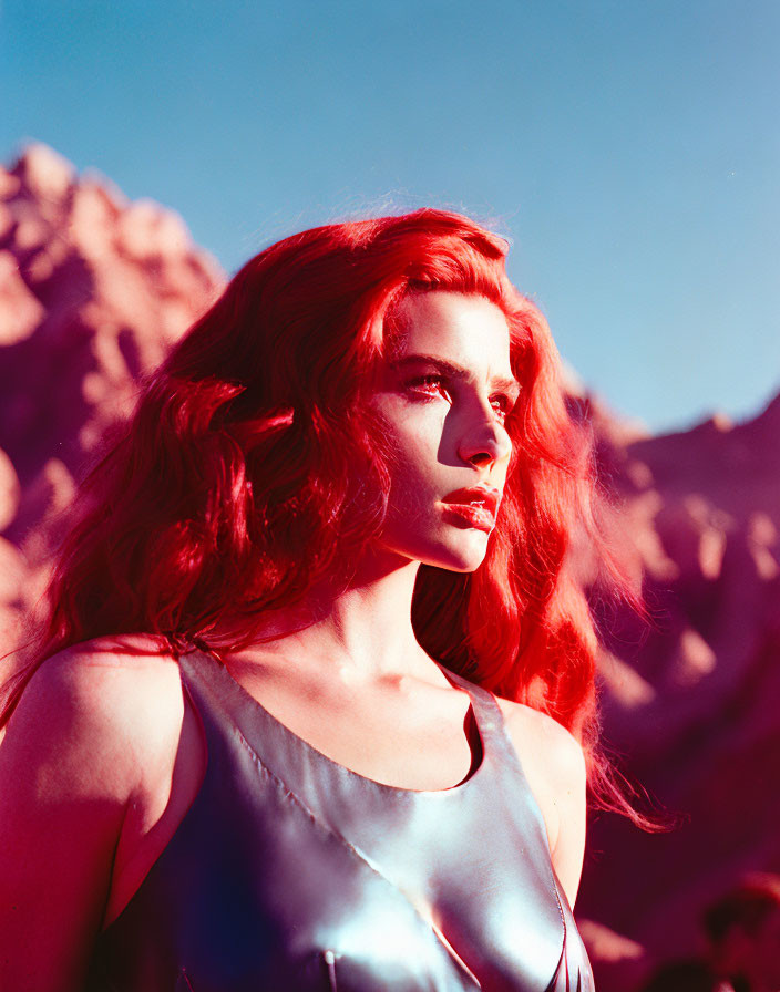 Red-haired woman in blue dress gazes in rocky landscape