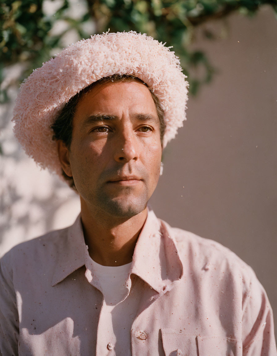 Man in Pink Shirt and White Fluffy Hat Against Wall with Shadows