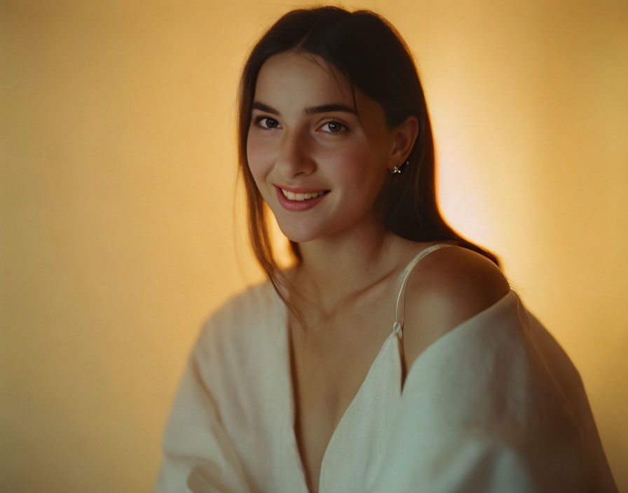 Dark-haired young woman in white top on soft orange backdrop