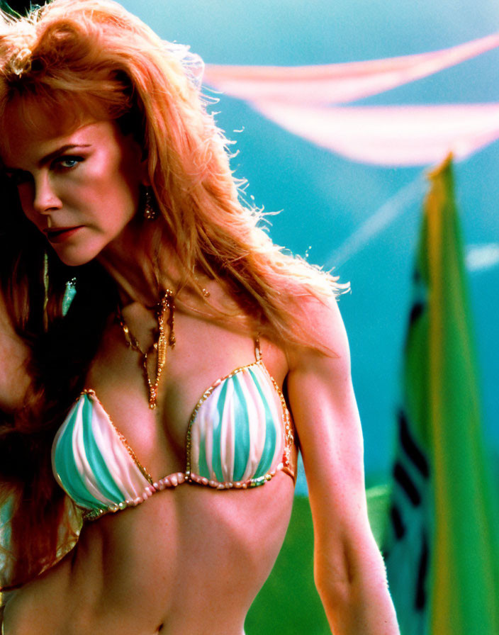 Red-haired woman in striped bikini top with beads, standing confidently amidst colorful fabric and flags.