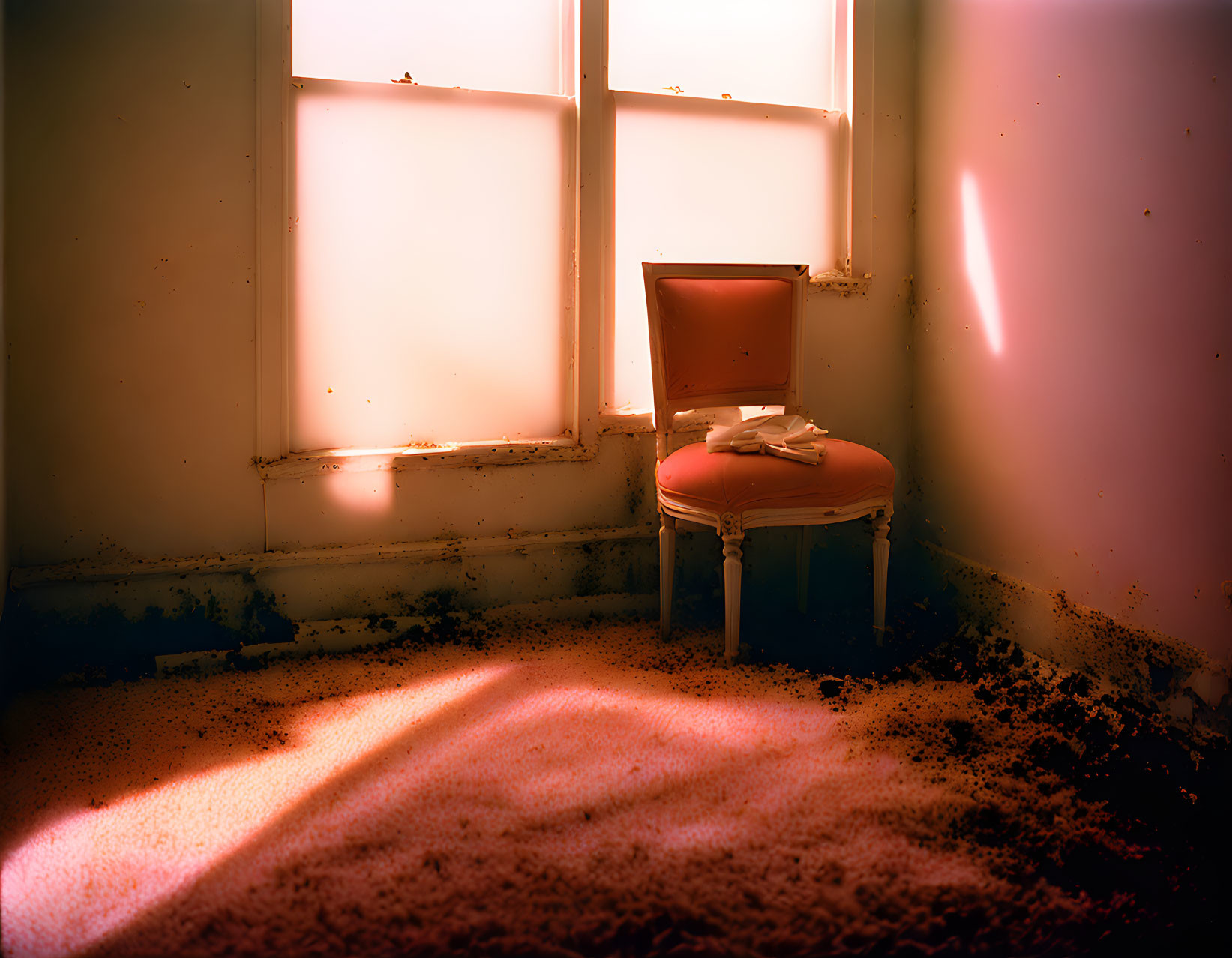 Vintage chair in sunlit room with peeling walls and debris.