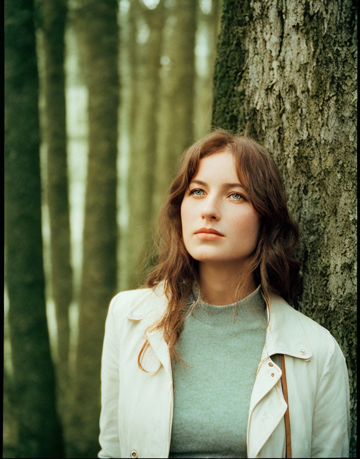 Serene young woman leaning against tree in forest