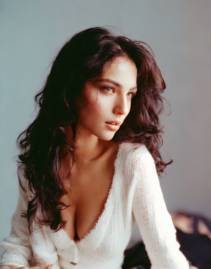 Dark-haired woman in white open-knit sweater gazes sideways