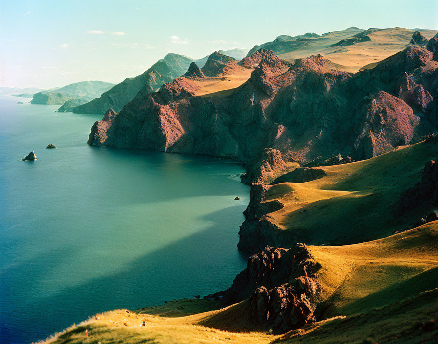 Tranquil landscape with rolling hills, cliffs, calm bay, and clear blue waters