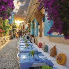 Classic car parked on vibrant street with colorful buildings and lush trees at sunrise or sunset