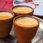 Three clay cups with liquid on reflective surface