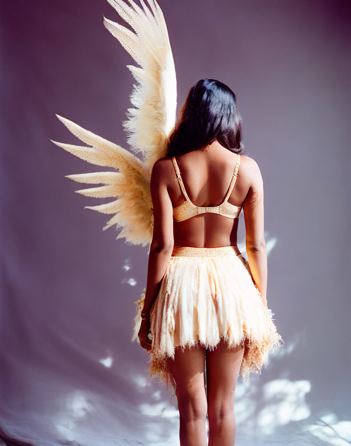 Woman in golden bralette and skirt with angel wings.