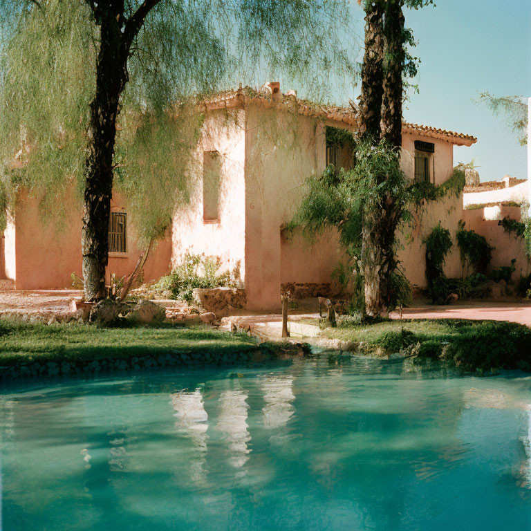 Tranquil blue pool with rustic terracotta house and green trees