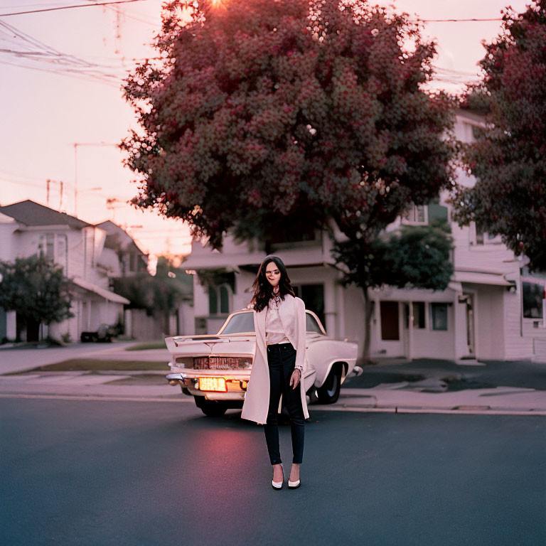 Woman standing in street at dusk with classic car and houses in background