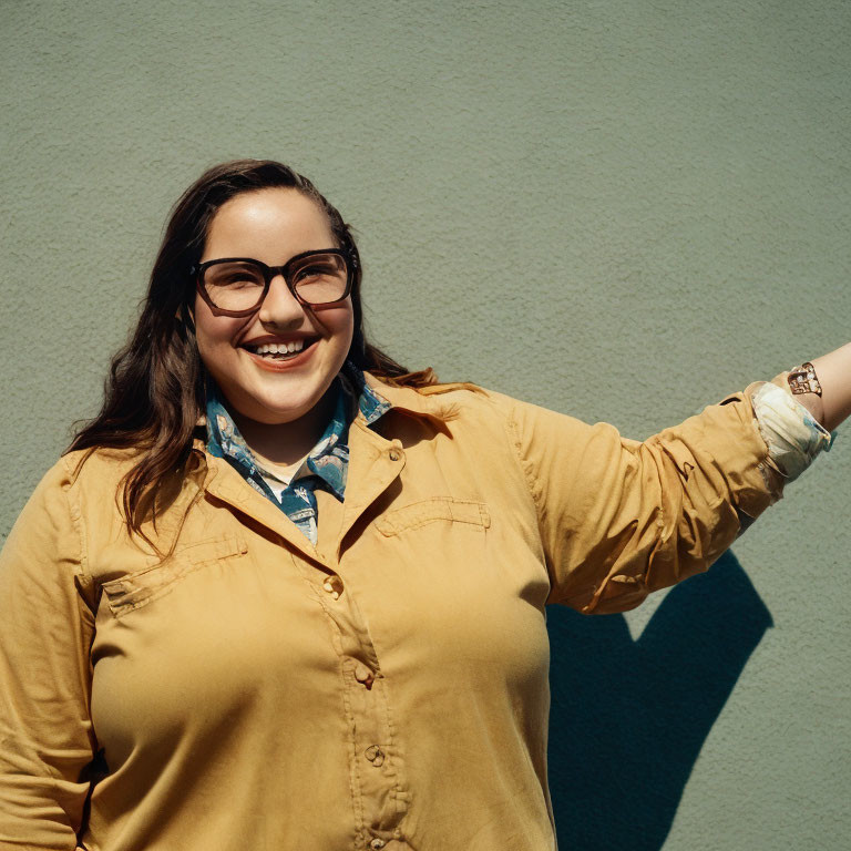 Smiling woman in yellow shirt against green wall with shadow