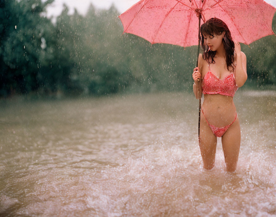 Person standing in rain with pink umbrella, red swimsuit, and water droplets.