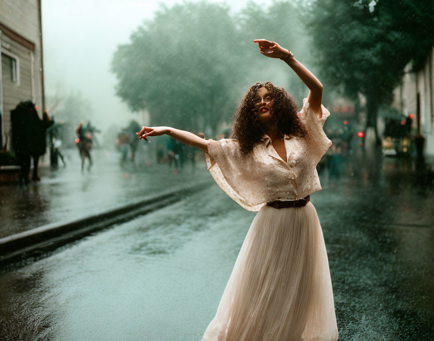 Woman in white dress dancing in rain on city street with blurred passersby.