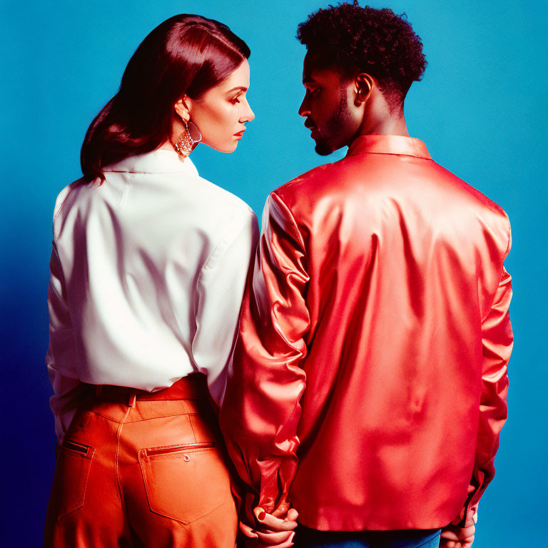 Two people in shiny red and white-orange outfits back to back on blue backdrop