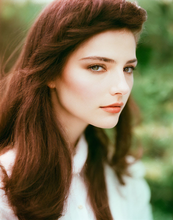 Portrait of woman with brown hair and fair skin in white shirt against natural backdrop