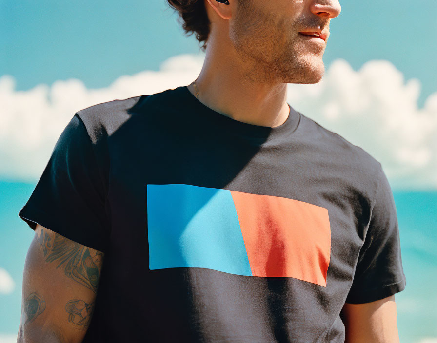 Man in Black T-Shirt with Blue and Red Design Against Cloudy Sky