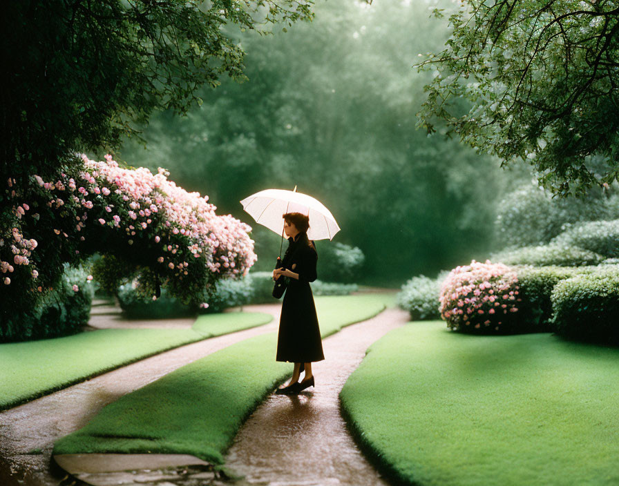 Woman with umbrella strolling garden path among lush greenery and pink flowers.