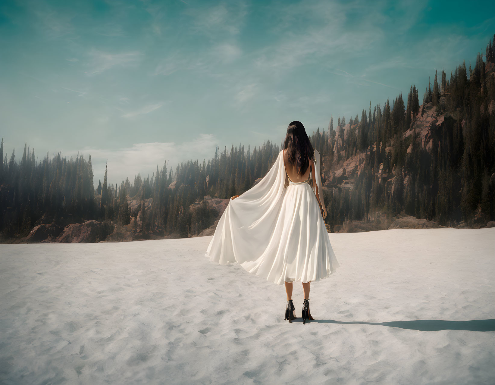 Woman in white dress and black boots in snowy landscape with forest and hazy sky