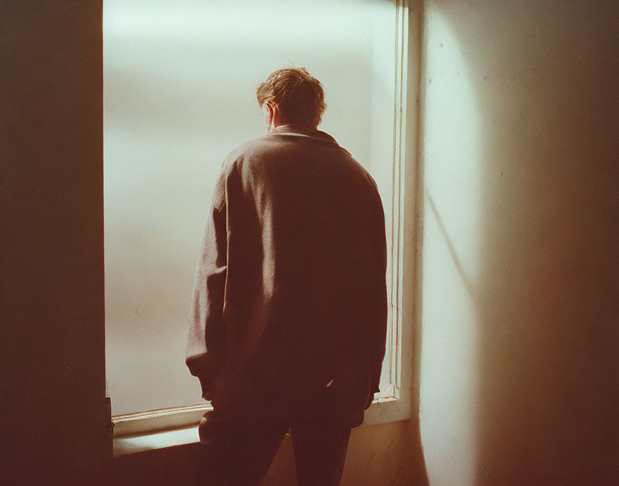 Person in Loose Sweater Contemplating View from Dimly Lit Room