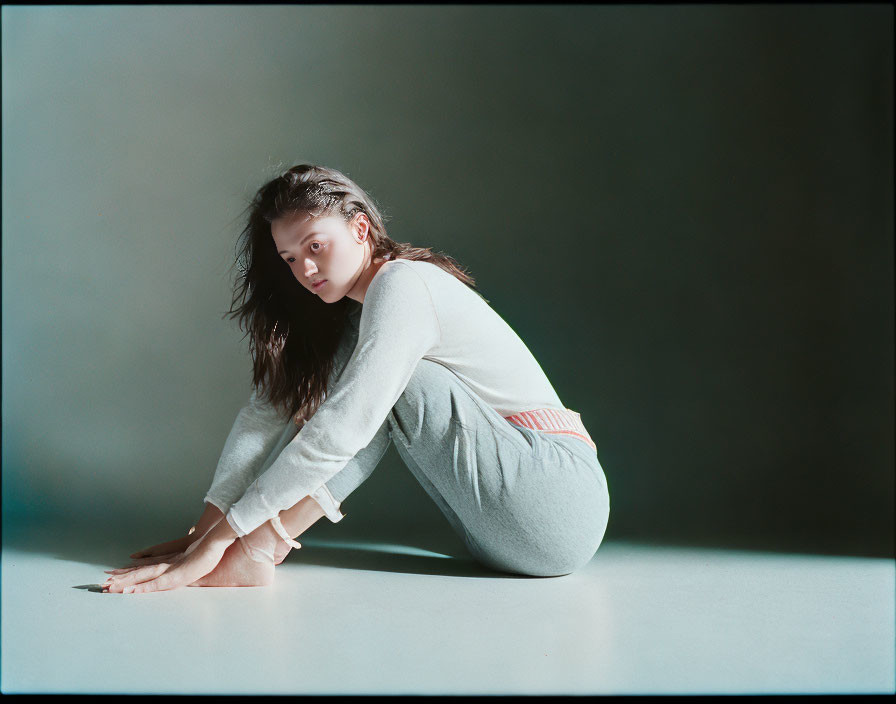 Person in grey outfit crouching on floor in thoughtful pose