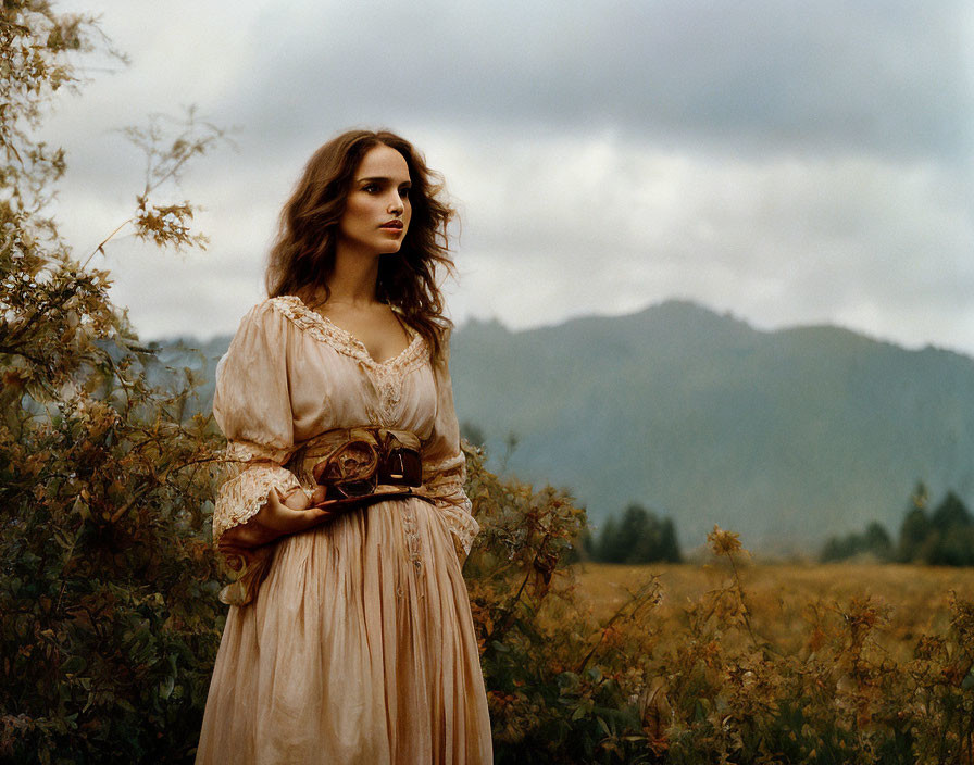 Vintage-dressed woman in field with mountains.