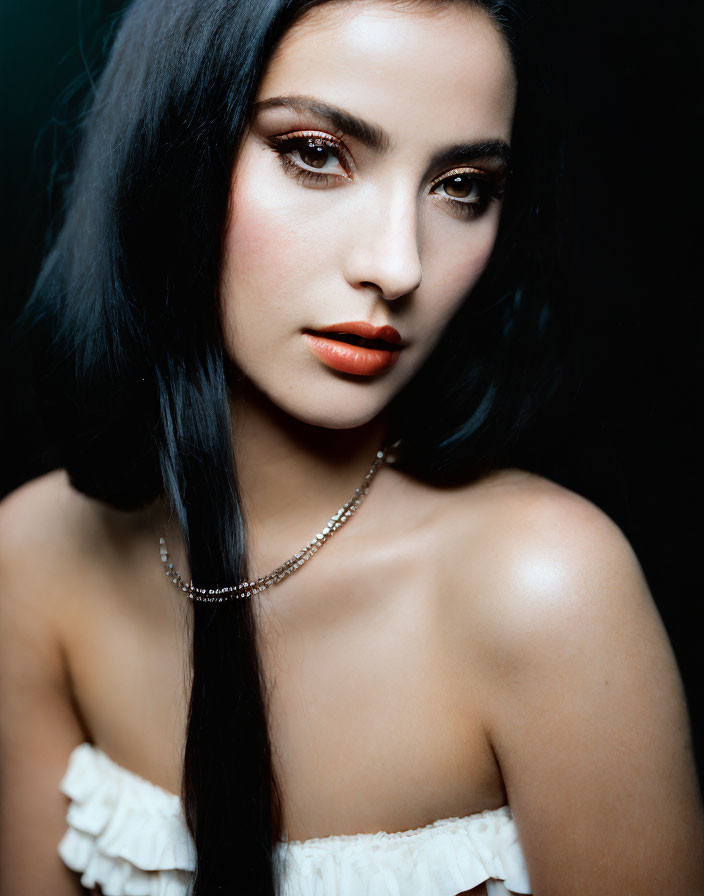 Dark-haired woman with red lipstick in off-shoulder top and necklace on dark background