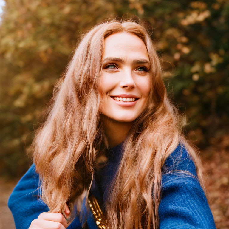 Smiling woman in blue sweater with wavy hair outdoors among autumn leaves