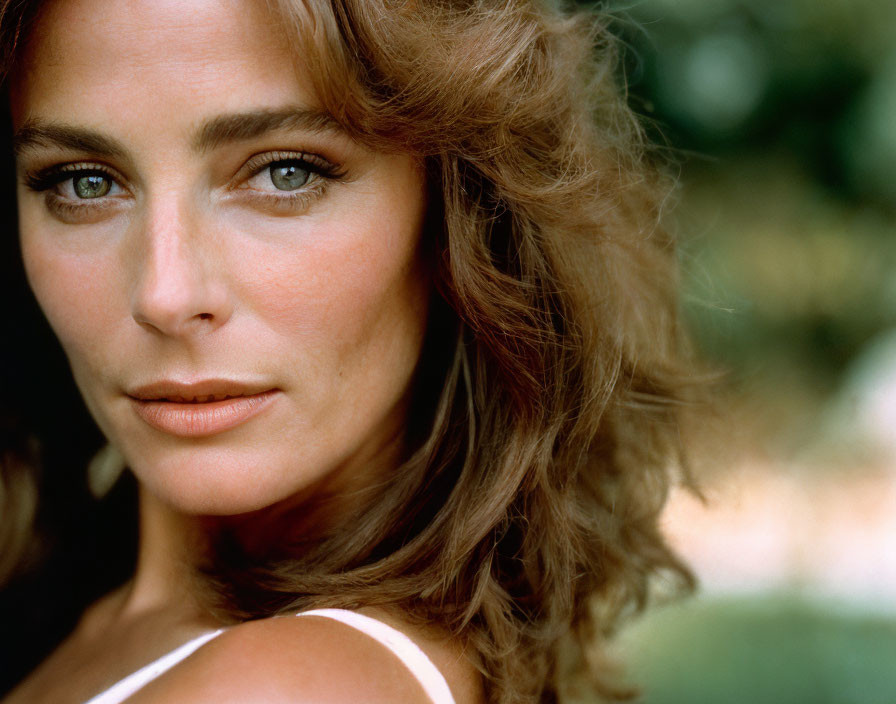 Portrait of a woman with hazel eyes and wavy brunette hair outdoors.