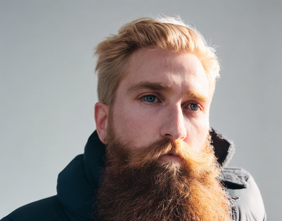 Bearded man with blue eyes in jacket on grey backdrop