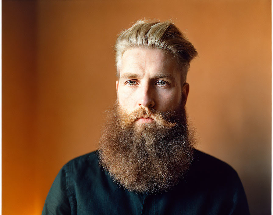 Serious man with full beard and styled hair on orange background