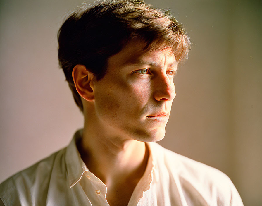 Person with short hair in profile wearing light-colored shirt against soft-lit background