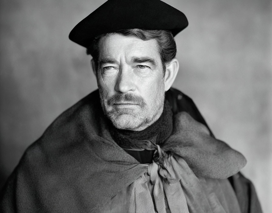 Monochrome portrait of a bearded man in beret and cloak