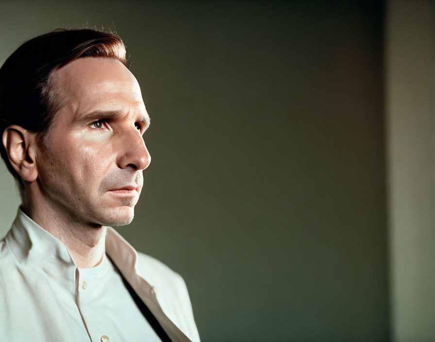 Man in Light-Colored Shirt and Dark Tie Poses Pensively on Green Background