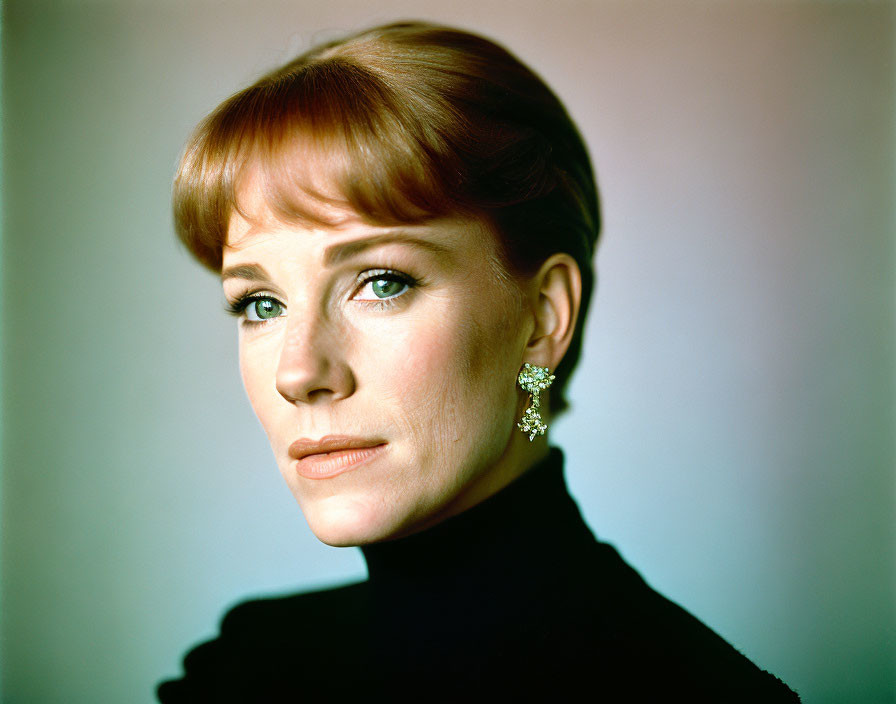 Red-haired woman in black turtleneck and elegant earrings gazes at camera