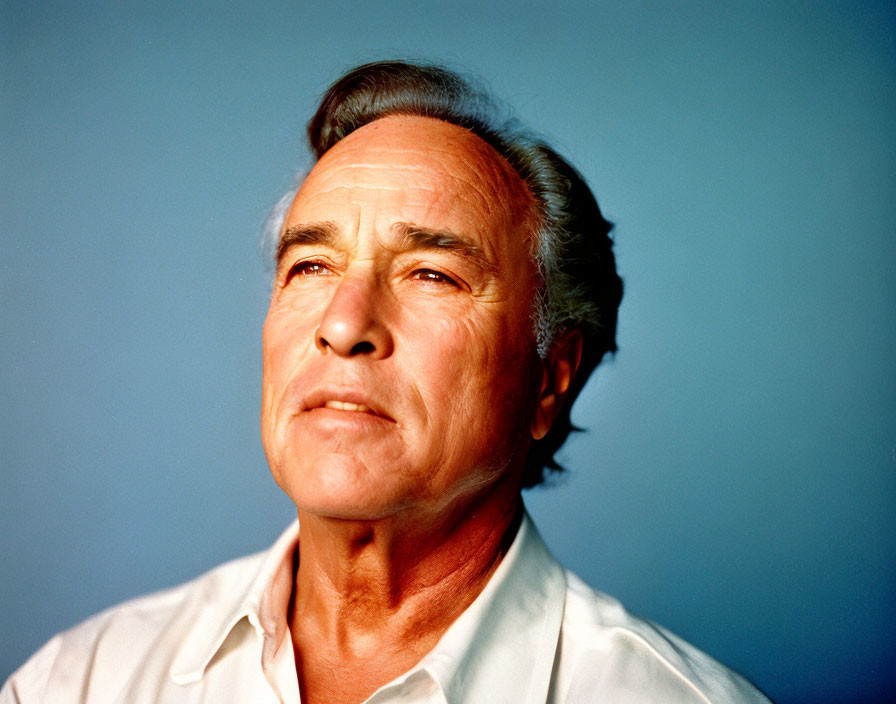 Grey-Haired Man in White Shirt Gazing Thoughtfully on Blue Background