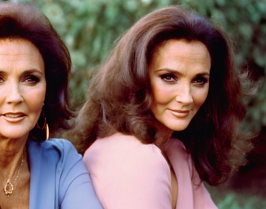 Two women with voluminous hair in elegant attire against greenery.