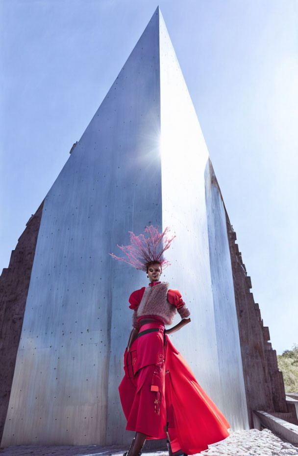 Avant-garde red outfit with headpiece at metal monument under blue sky