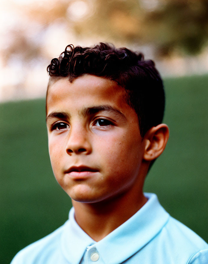 Curly-Haired Boy in Blue Polo Shirt Outdoors with Trees