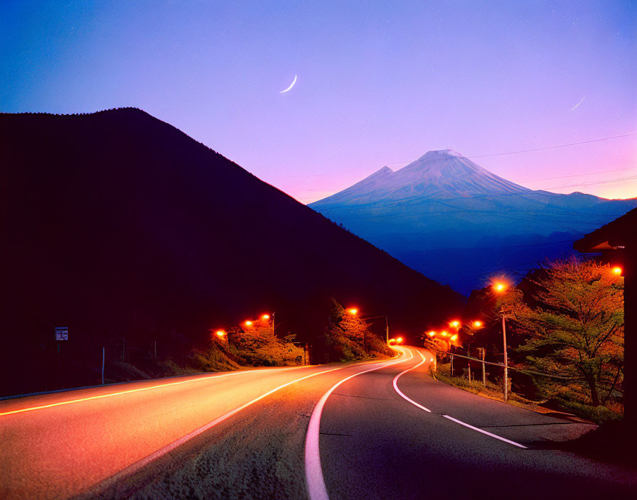 Twilight road with streetlights leading to Mount Fuji under crescent moon