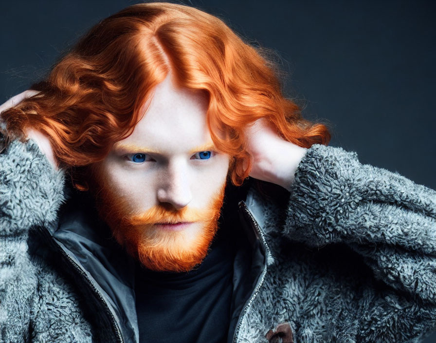 Striking red-haired person with blue eyes in furry jacket pose on dark background