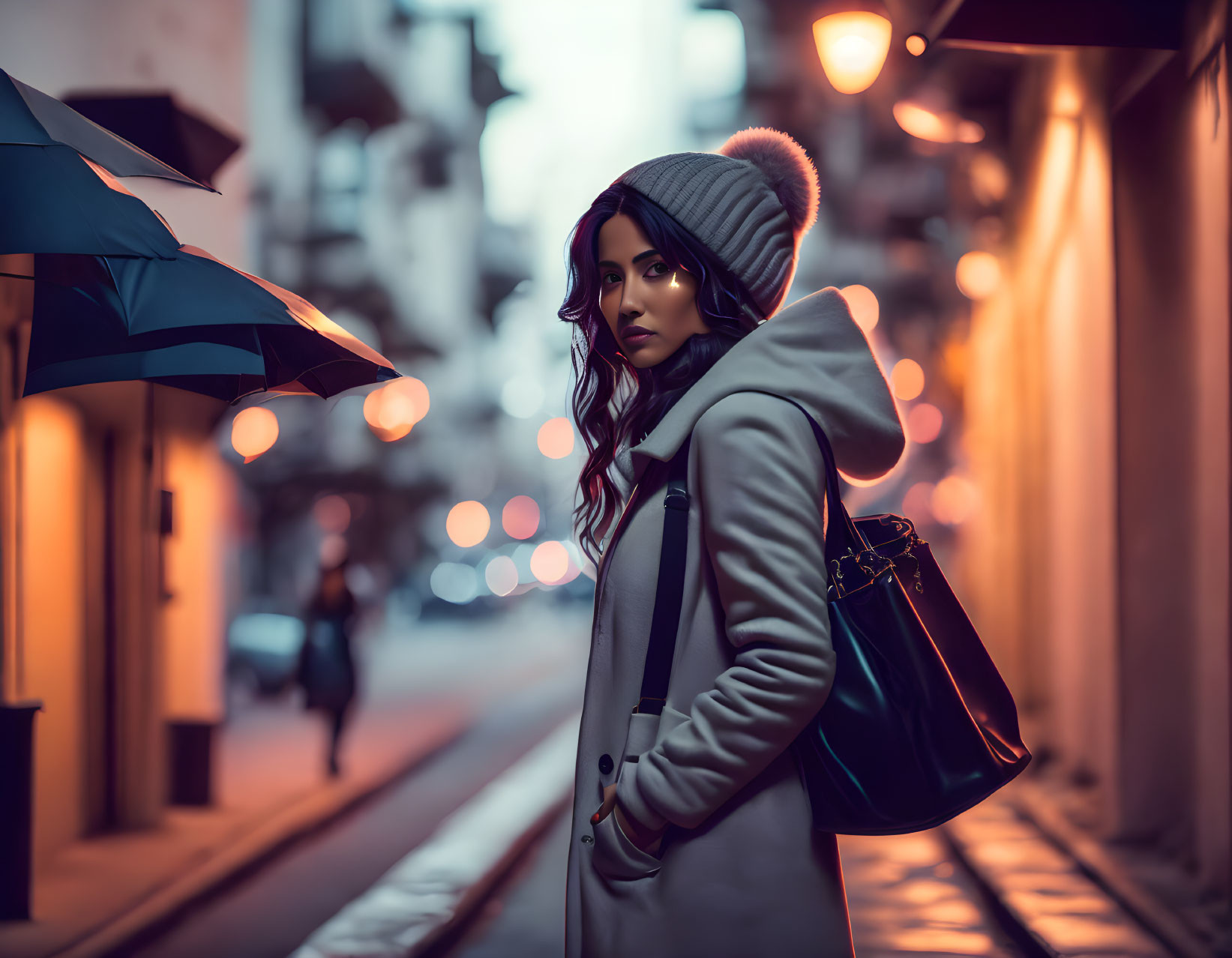 Woman in winter coat and beanie on city street at dusk with glowing street lights