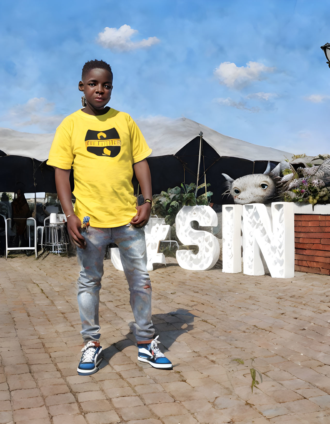 Young person in yellow t-shirt and distressed jeans with decorative letters and sculpture in background