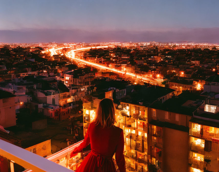 Woman in red dress on balcony at dusk with cityscape view.