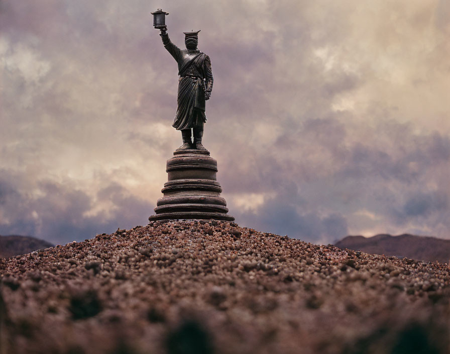 Robed Figure Statue Holding Torch on Pebbled Mound