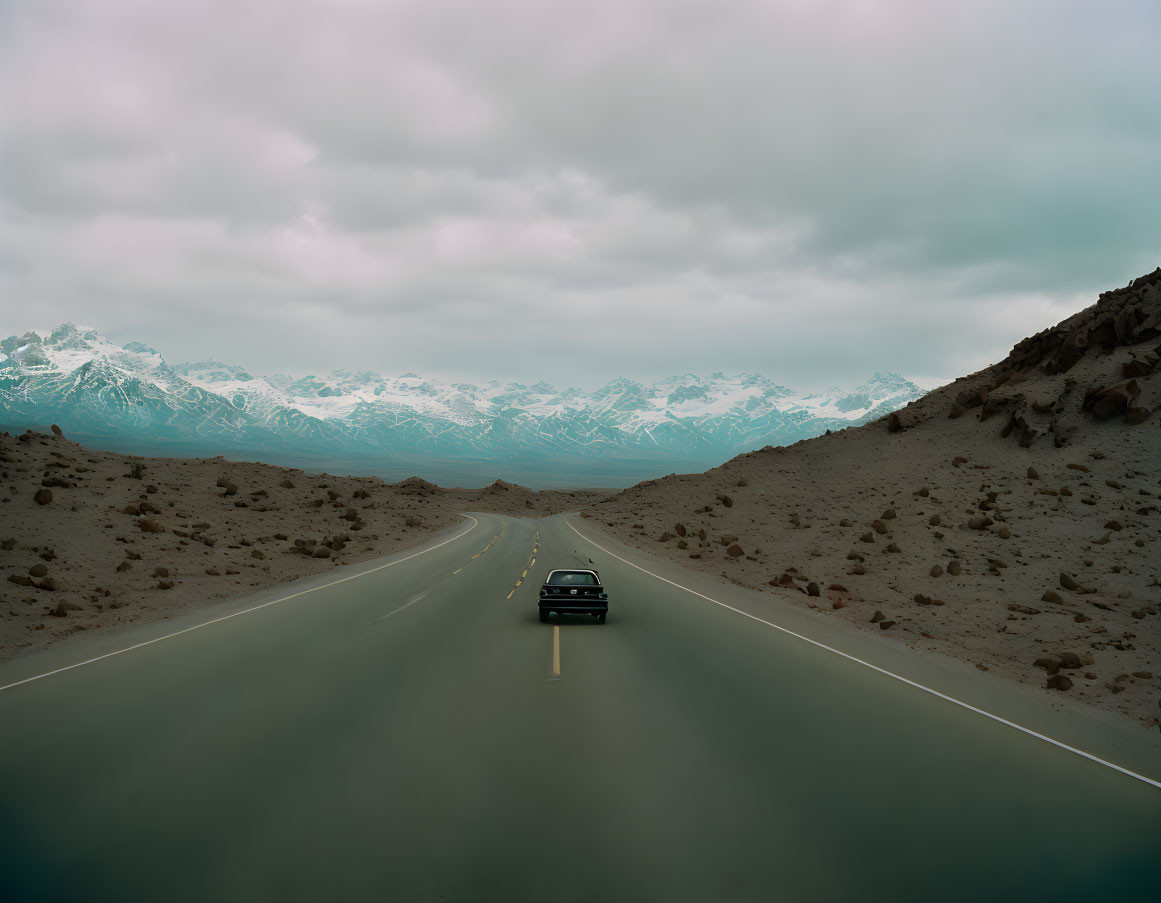 Solitary car on straight road towards snowy mountains